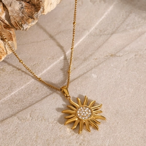 Détail du collier pendentif soleil doré avec zircons étincelants sur une surface en pierre