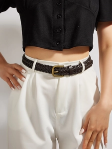 Detailed view of deep brown woven belt with bronze buckle on white high-waist trousers
