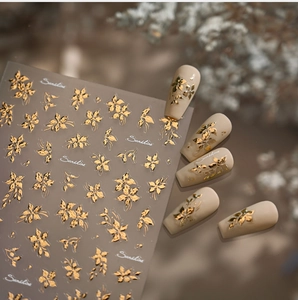 Close-up of gold flower nail stickers and 3D floral application on matte nude nails