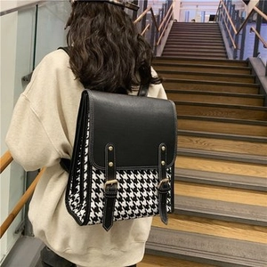 Detail of checkered backpack with dual buckle straps shown on model in a modern interior