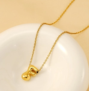 Detailed view of bubble initial F pendant necklace with shiny golden finish on ceramic