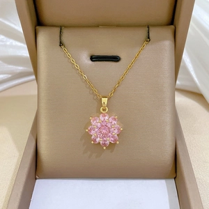 Detailed close-up of a golden necklace with a pink flower pendant set in a jewelry box