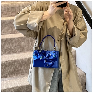 Detailed view of deep blue satin evening bag with crystal bow and gold chain strap