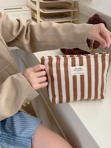 Brown and white striped large capacity makeup bag held by hand in a lifestyle setting