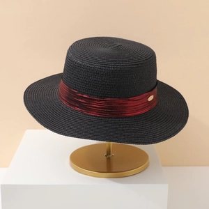 Minimalist black straw boater hat with burgundy ribbon and gold logo on metal stand