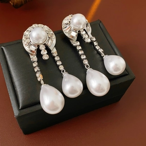 Close-up of silver drop earrings with white pearls and sparkling rhinestones on black leather