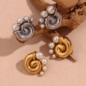 Detail of spiral twisted earrings in gold and silver finish with pearls on wood