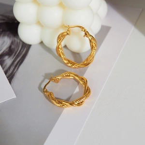 Luxurious gold twisted hoop earrings with fringe tassels on white textured background