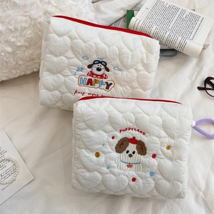 Detail of white quilted cosmetic bags featuring cute puppy embroidery and red zipper
