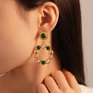 Vintage gold earrings with green gemstones and clear crystals worn by a model