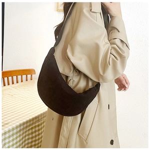 Detail view of black corduroy crescent bag worn by a model in a minimalist indoor setting