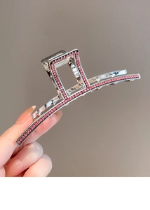 Detailed view of a silver shark hair claw clip with pink rhinestones held by hand