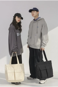Detail of multi-pocket canvas tote bags in cream and black shown by couple models