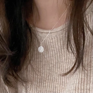 Irregular textured silver necklace pendant shown on a beige knit sweater background