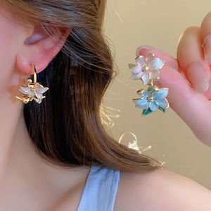 Detailed macro view of white and light blue enamel flower earrings with gold-plated finish
