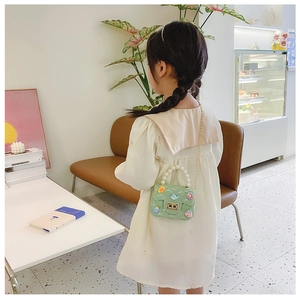 Girl wearing green mini crossbody bag with pearl handle and cartoon charms in a cafe