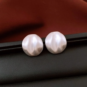 Macro detail of silver oval stud earrings with brushed texture on black leather surface