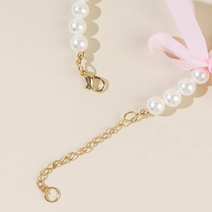 Detail of pet pearl necklace with golden lobster clasp and pink silk ribbon bow