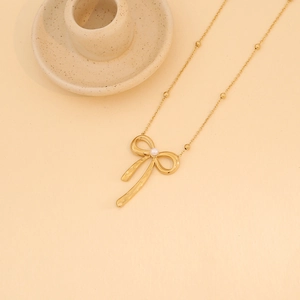 Detail of a golden bow pendant with a small pearl inlay on a fine beaded necklace chain