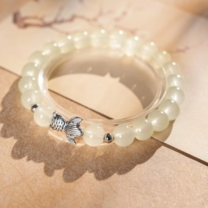 Macro detail of jade bead bracelet with silver fish pendant on an artistic shadow background