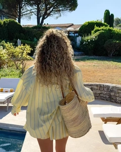 Back view of a loose striped shirt set with a straw bucket bag by a sunny poolside