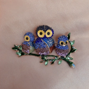 Macro shot of owl brooch with blue crystals and green enamel on branch detail