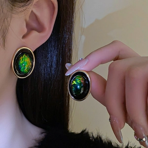Vue détaillée de boucles d'oreilles ovales en résine verte avec bordures dorées sur modèle