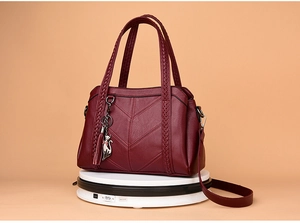 Close-up of wine red PU leather handbag with V-quilting, woven handle and cat charm