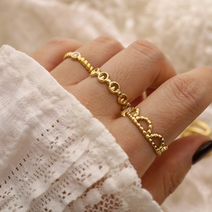 Close-up of three 18K gold-plated rings including heart and chain designs on a model