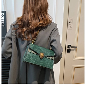 Detail of green crocodile texture flap bag with a golden lion head clasp and chain