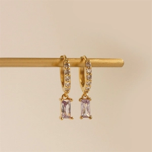 Close-up of gold hoop earrings featuring white zircons and rectangular lilac gemstone pendants
