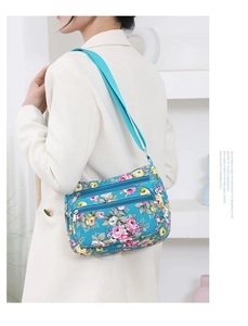 Detail of floral printed crossbody bag with multi-layer zippers on blue canvas base