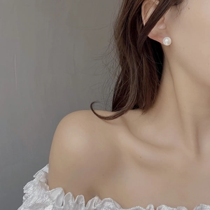 Close-up of a high-luster round white pearl earring worn by a model for a retro look