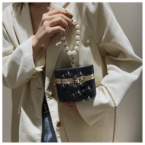Detail of black cylindrical pearl handbag with rhinestones worn on a beige blazer