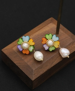 Detailed macro view of pearl floral earrings with multicolored heart petals and wood stand