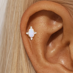 Close-up of golden S925 silver earring with oval opal and zircon accents on ear