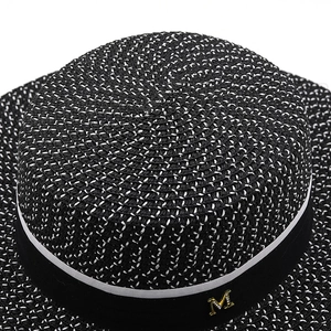 Macro detail of black and white woven texture on a boater hat with a gold metal M logo
