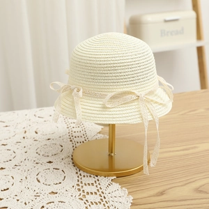 Detail of children's straw hat with white lace bow on a golden display stand