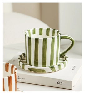 Detail of hand-painted green striped ceramic coffee cup and saucer set on a white book