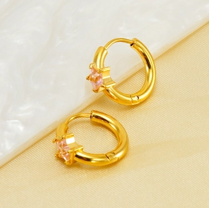 Gros plan de boucles d'oreilles créoles dorées avec étoile en zircon rose et métal brossé