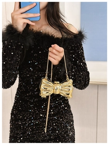Close-up of golden bow-shaped evening bag with glossy metallic finish and fine chain