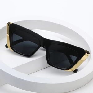 Fashionable cat-eye sunglasses with black frames and gold metal trim on a white pedestal