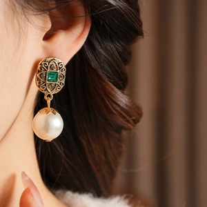Dettaglio di orecchini vintage con gemma verde e grandi pendenti di perle bianche