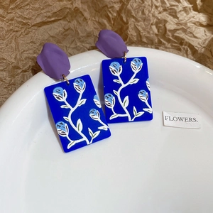 Detail of floral earrings with purple flower studs and blue rectangular painted pendants