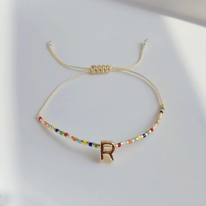 Detailansicht eines Boho-Webarmbands mit bunten Perlen und goldenem Buchstaben-R-Anhänger