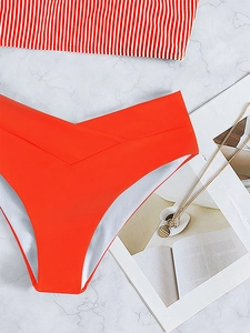 Flat lay of high-waisted orange bikini bottoms with striped top and fashion magazine detail