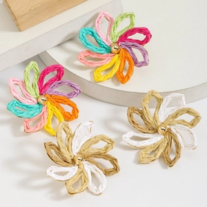 Close-up of handmade raffia flower earrings with golden beads on geometric stands
