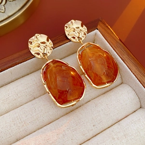 Close-up of irregular amber resin earrings with golden metal base on a wooden box