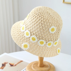 Beige woven straw sun hat with daisy flower appliques on a minimalist wooden display stand
