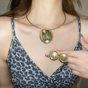Detailed close-up of golden oval pendant necklace and round stud earrings set on model